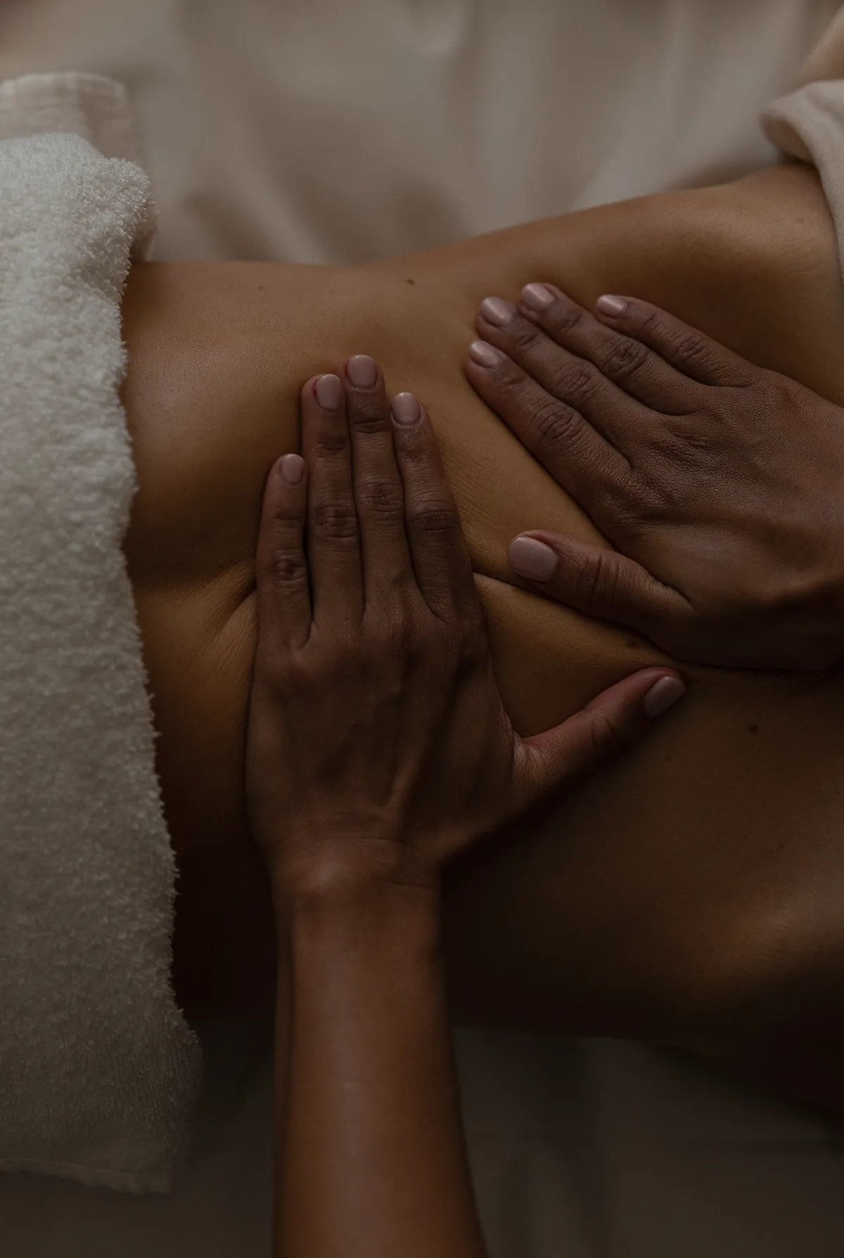 Both hands working in long strokes across a client’s back, a folded towel alongside.