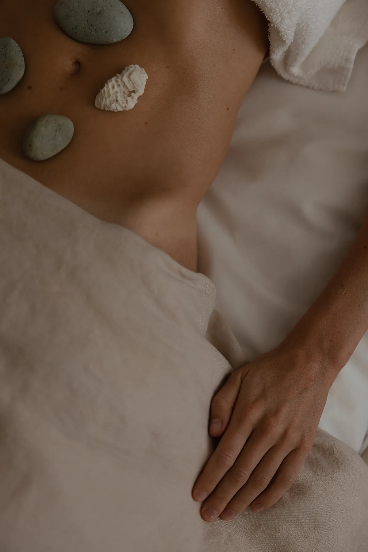 Smooth green stones and a piece of white coral laid across a client’s body on the treatment table.