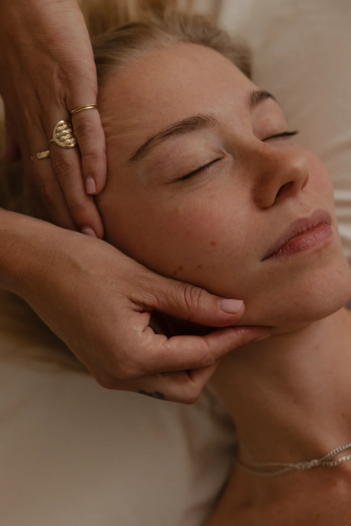 Two hands cradling and sculpting along the jawline of a client during a facial massage.