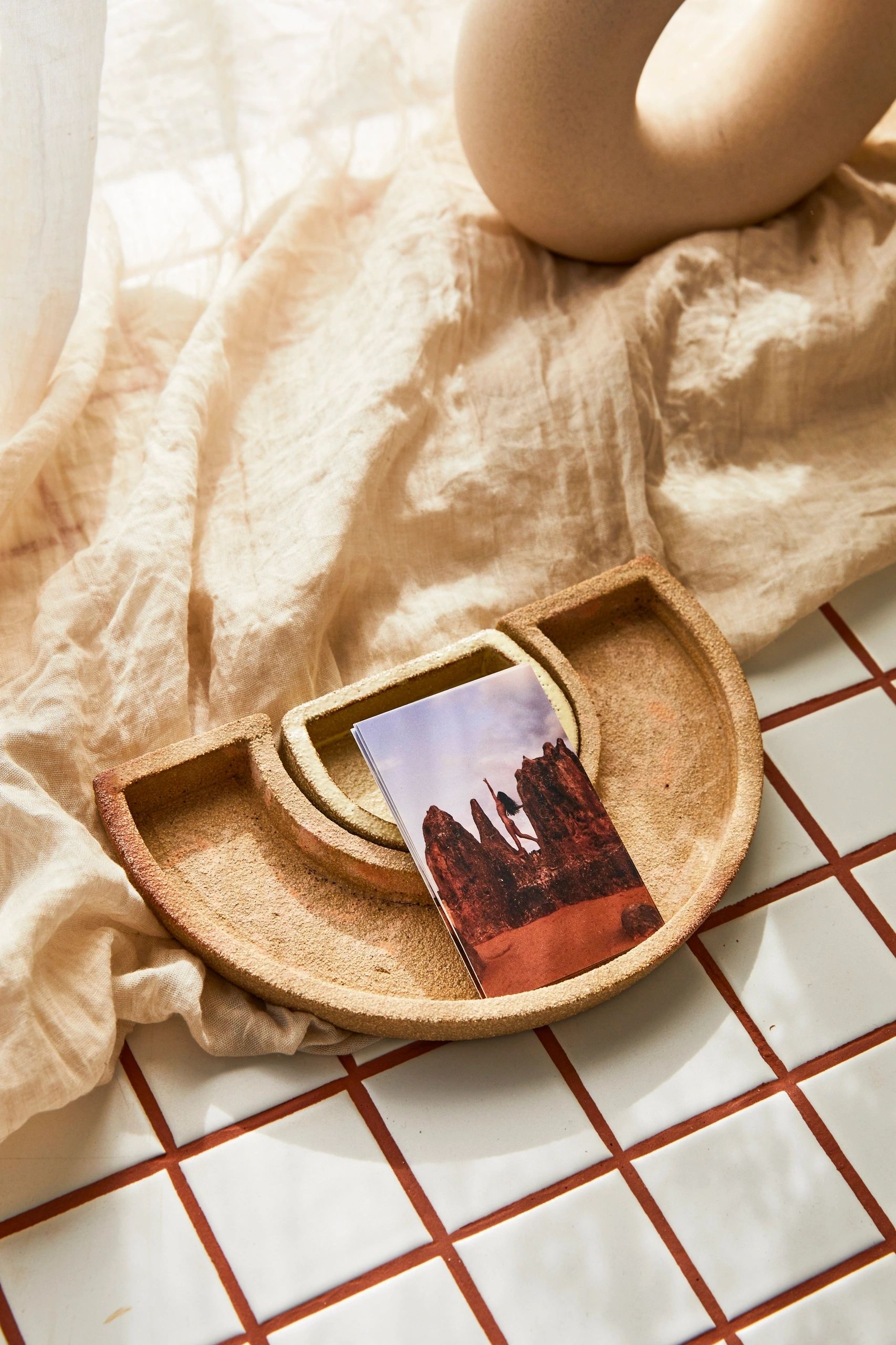Monica Pronk’s postcard prints resting in a sculptural ceramic tray on white tiles at the Mesa studio.